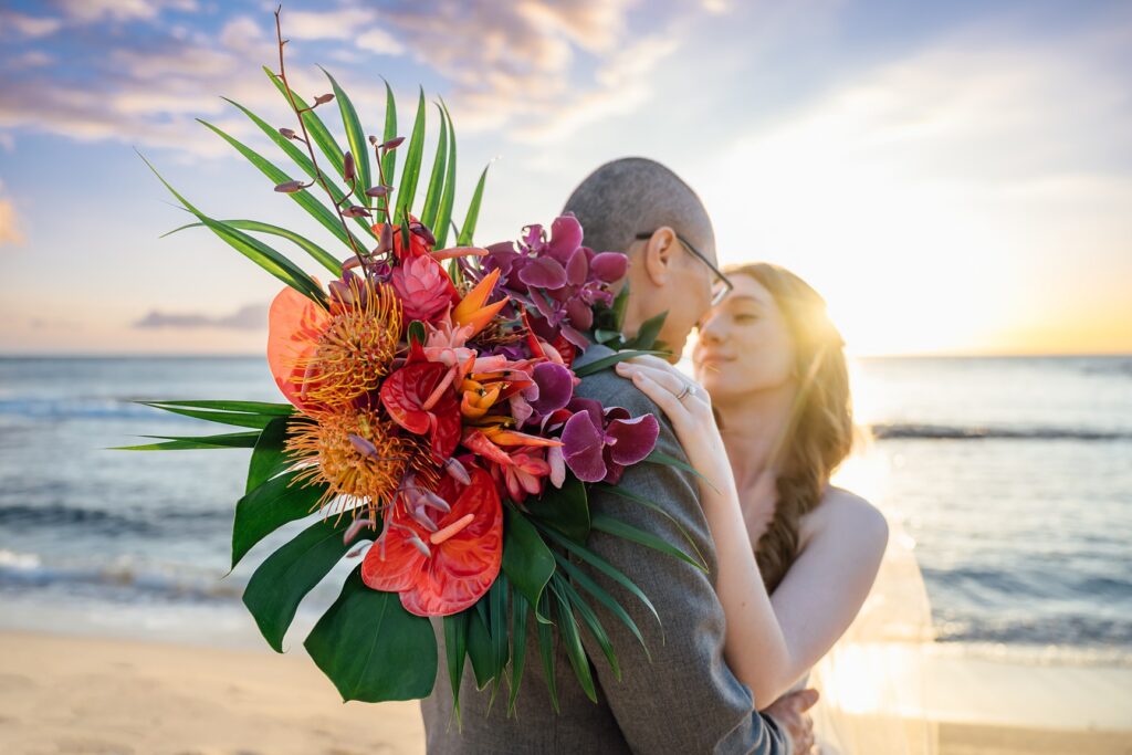 Newlywed couple holding hands along a lava rock coastline during golden hour on the Big Island